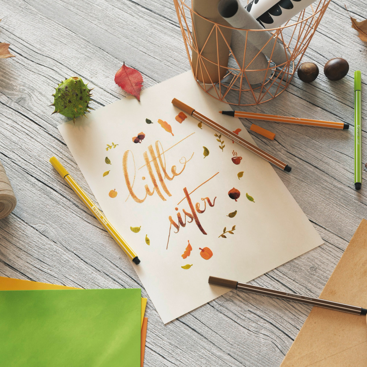 Pen 68 auf einem Holztisch mit herbstlichem Lettering "little sister", umgeben von bunten Stiften und Blättern.