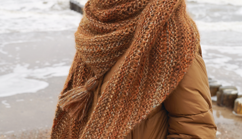 Strickanleitung Dreieckstuch aus Creative Mohair Melange: Frau am Strand mit braunem, gestricktem Tuch, das sie warm umhüllt.