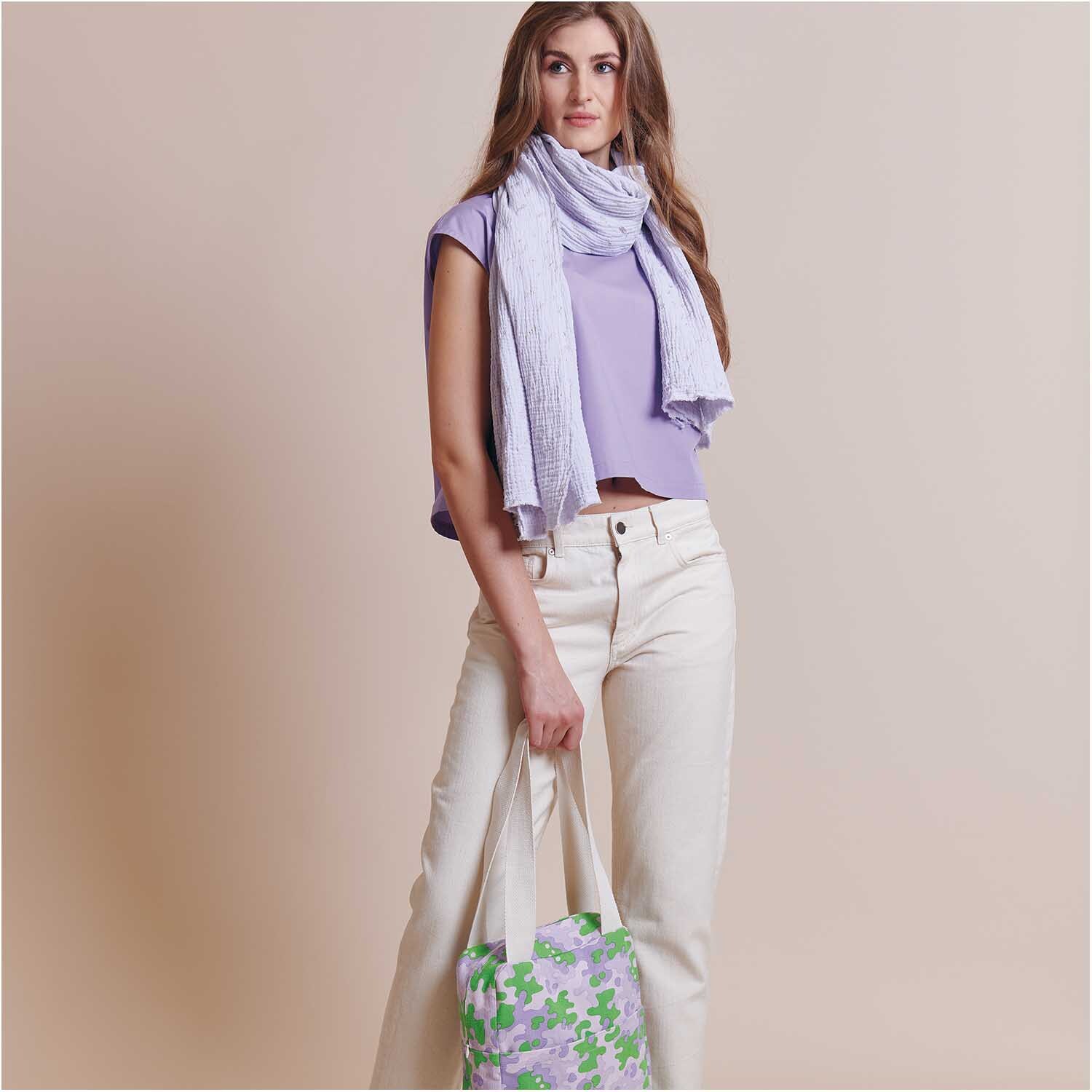 Stoffabschnitt Krinkelmusselin grau 50x130cm Hot Foil: Frau in lila Oberteil mit passendem Schal und gemusterter Tasche.