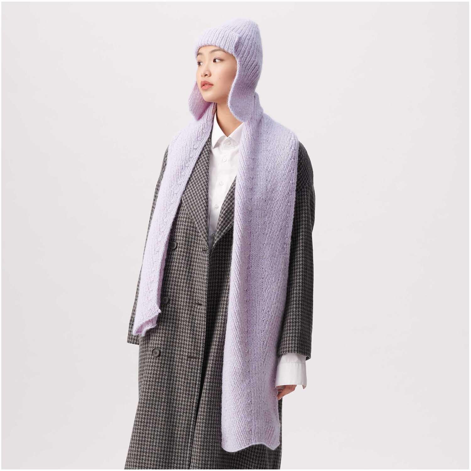Strickset Mütze Modell 13: Frau trägt lila Mütze und Schal über kariertem Mantel, stilvoll und modern.