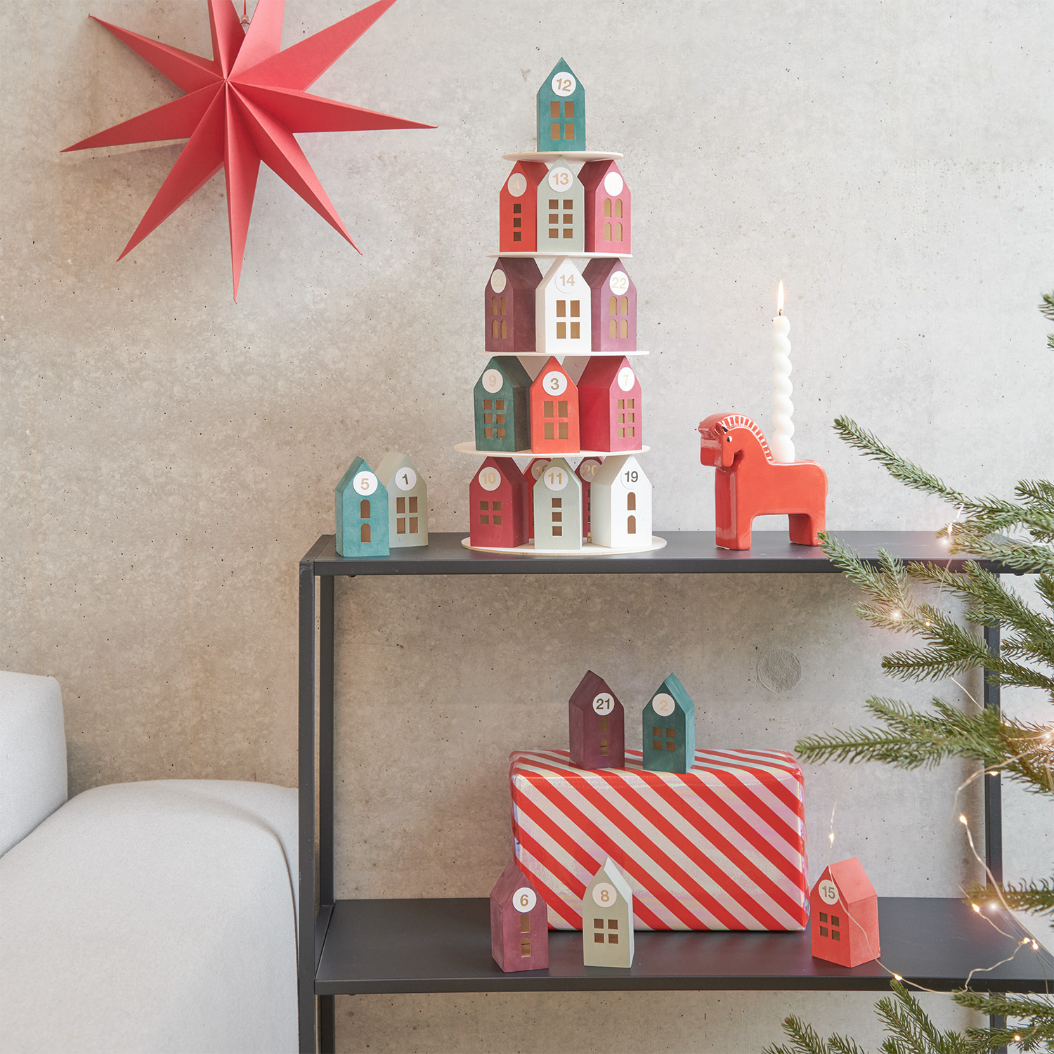 Anleitung Adventskalender Holz-Haus-Pyramide: Bunte Holzhäuser auf Regal, dekoriert mit rotem Stern und Kerze.