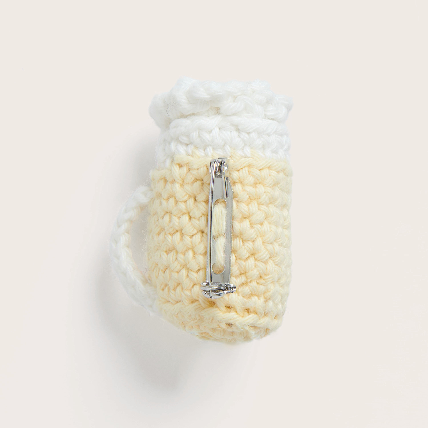Häkelset Maßkrug Modell 10: Ein cremefarbenes, gehäkeltes Maßkrug-Design mit Anstecknadel von Rico Design.