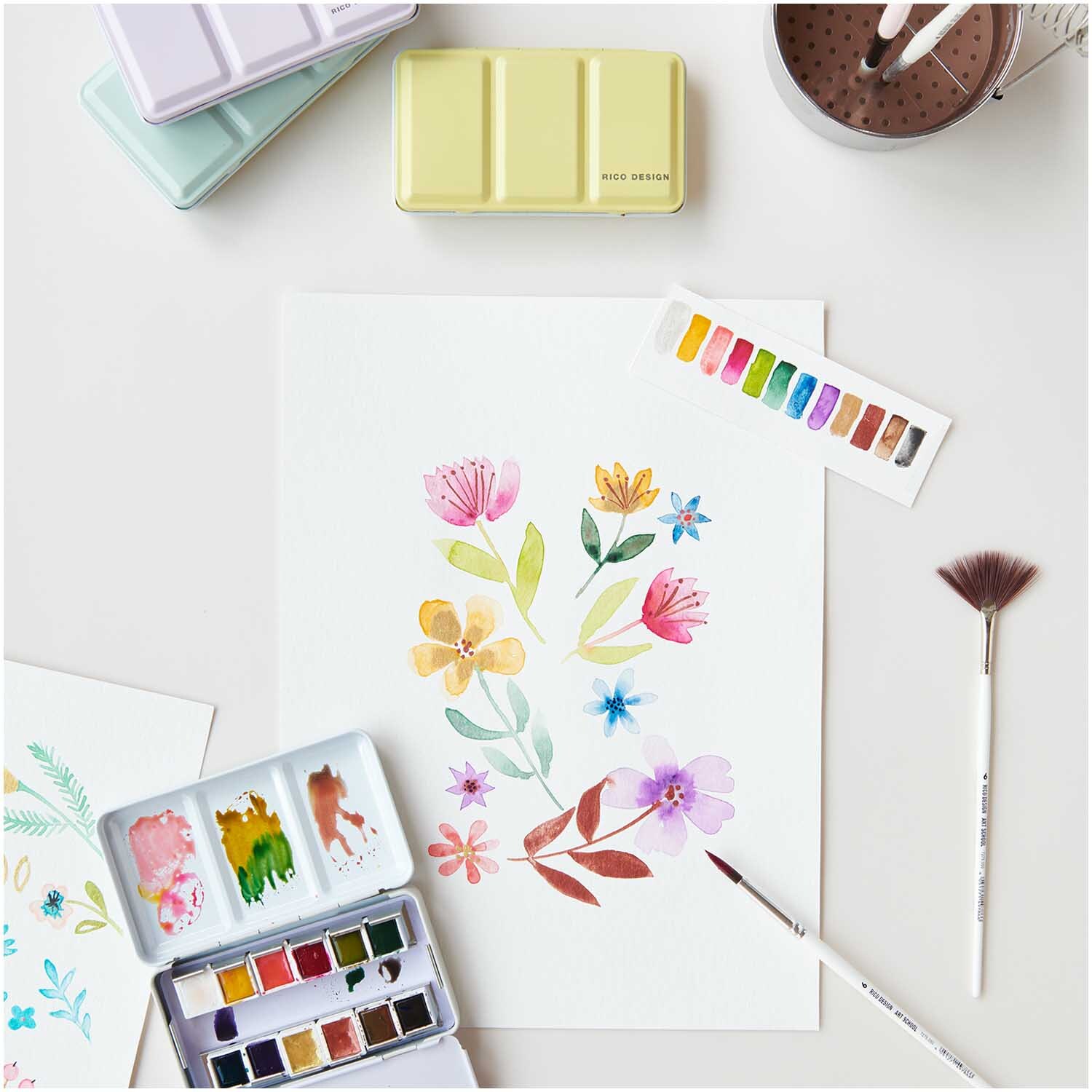 ART Master Aquarellfarben 12 Farben: Bunte Blumenillustration mit Aquarellset und Pinseln auf weißem Papier.