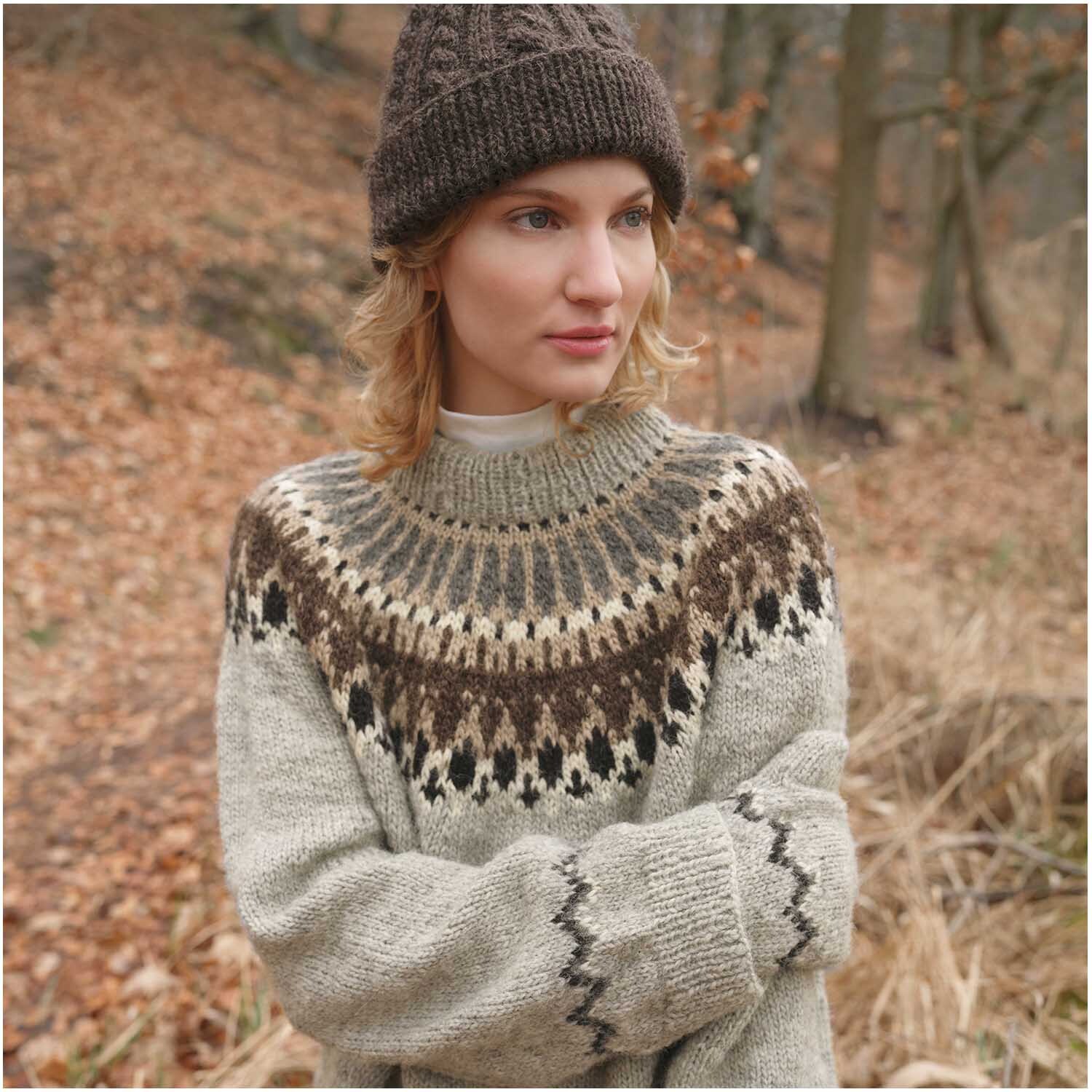 Strickset Mütze Modell 03 aus Luxury Knits Winter Special: Frau im Wald mit brauner Mütze und gemustertem Pullover in Naturtönen.