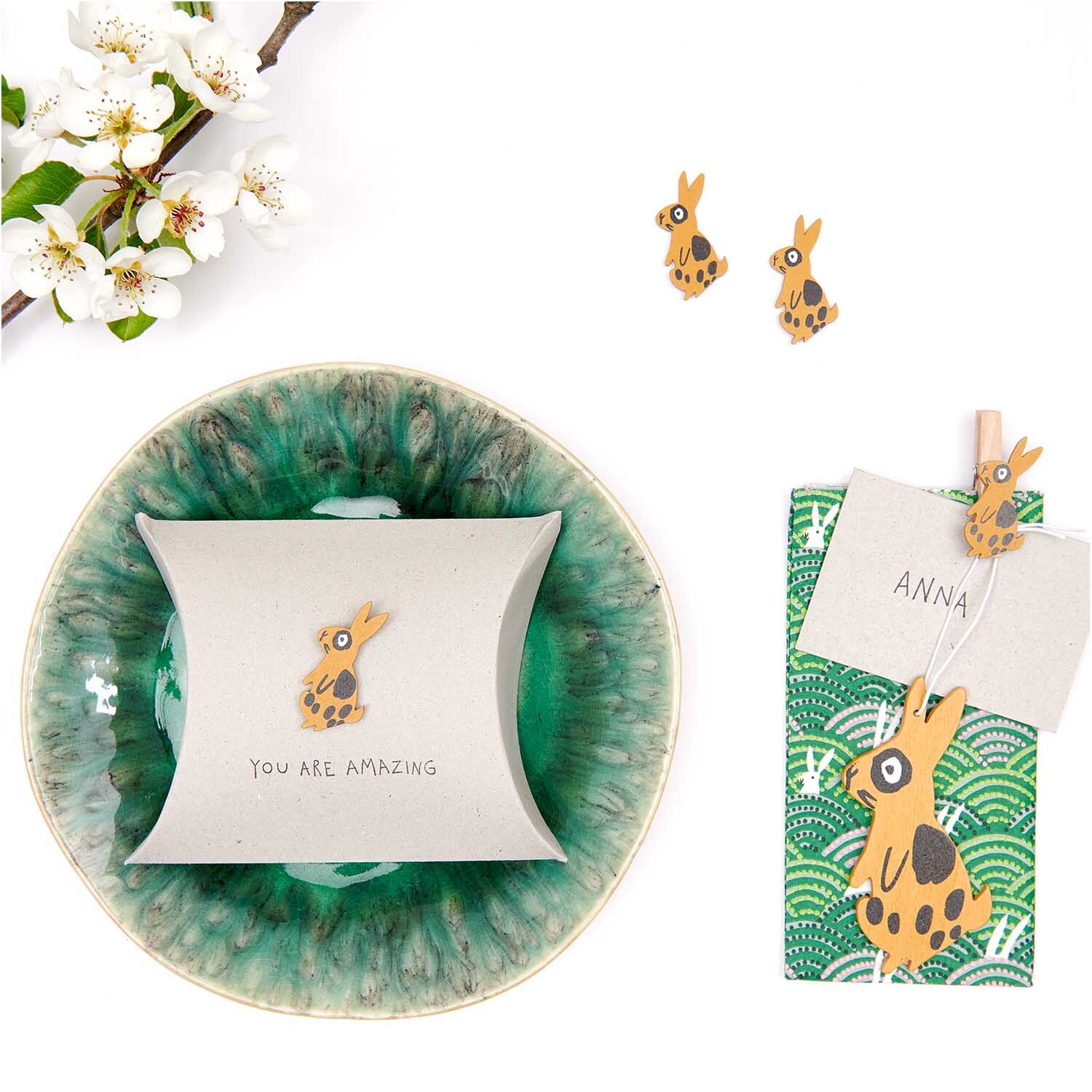Dekoklammern Hase braun 4 Stück von Rico Design auf grünem Teller mit Blumen und Geschenkkarte.