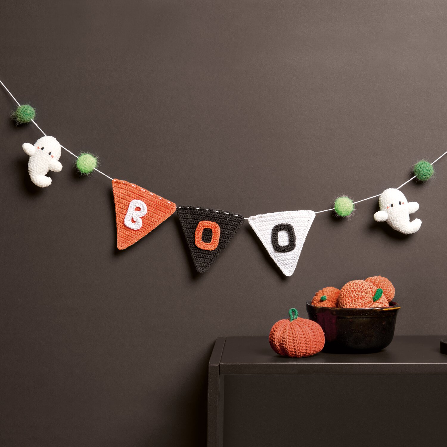 Ricorumi In the Meadow, gehäkelte Halloween-Girlande mit Gespenstern, Kürbissen, Wimpeln in Weiß, Schwarz, Orange und grünen Pompons, Deko an dunkler Wand