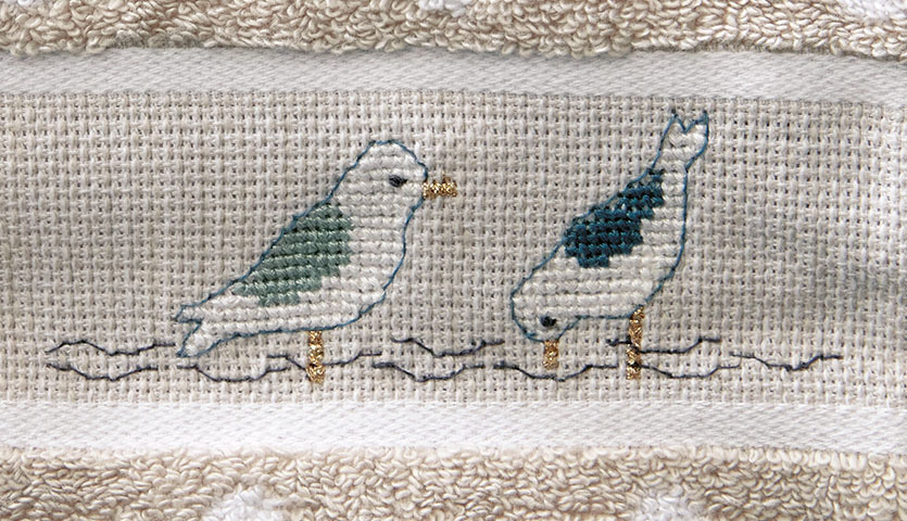 Stickanleitung maritimer Waschhandschuh mit gestickten Möwen auf beigem Hintergrund, ideal für Handarbeitsprojekte.