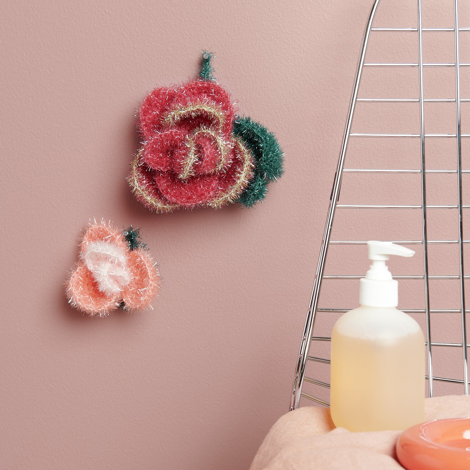 Häkelset Creative Bubble Rose Romantic: Zwei gehäkelte Rosen in Rosa und Grün an einer rosa Wand.