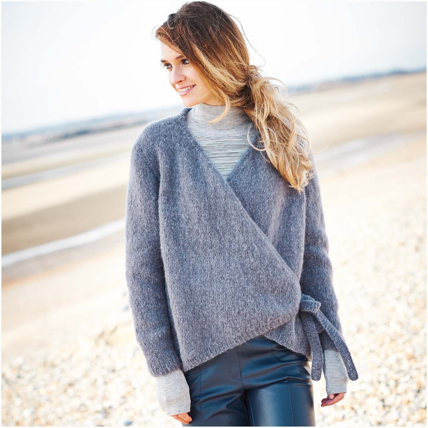 Luxury Volumi Strickjacke in Rauchblau von Rico Design, getragen von Frau am Strand.