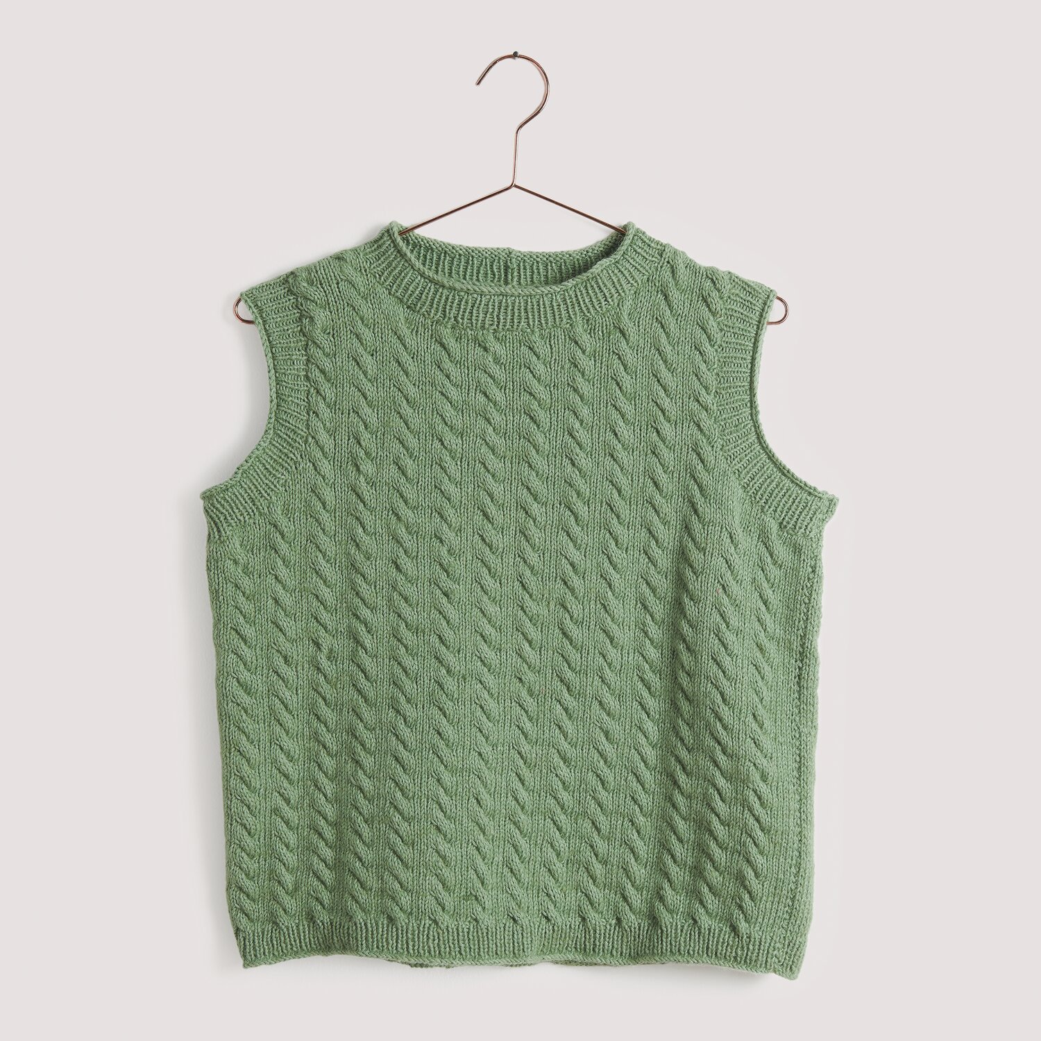 Strickset Top Modell 23 aus Die Neue Masche No. 15: Grünes, ärmelloses Strickoberteil mit Zopfmuster auf einem Kleiderbügel.