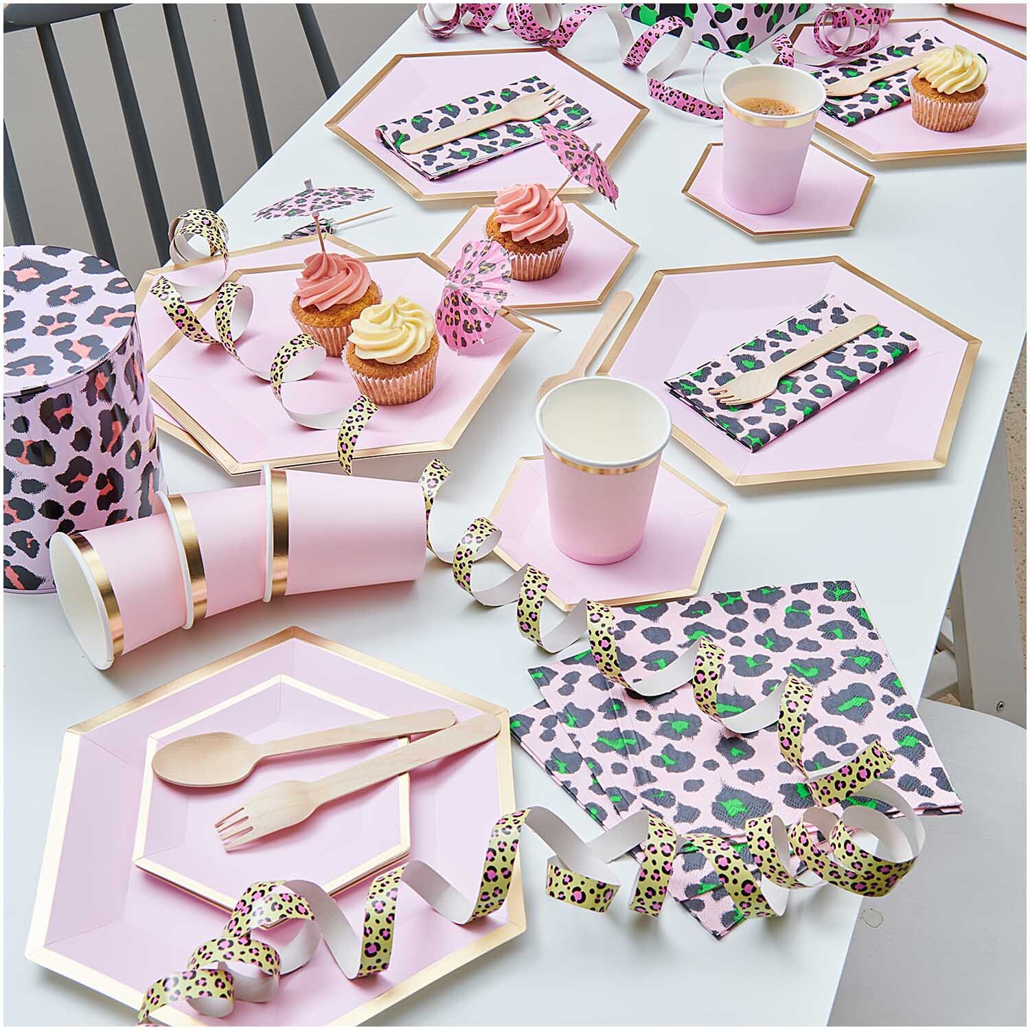 Pappteller Sechseck rosa-gold von Rico Design, dekoriert mit Partyzubehör und Cupcakes auf einem Tisch.