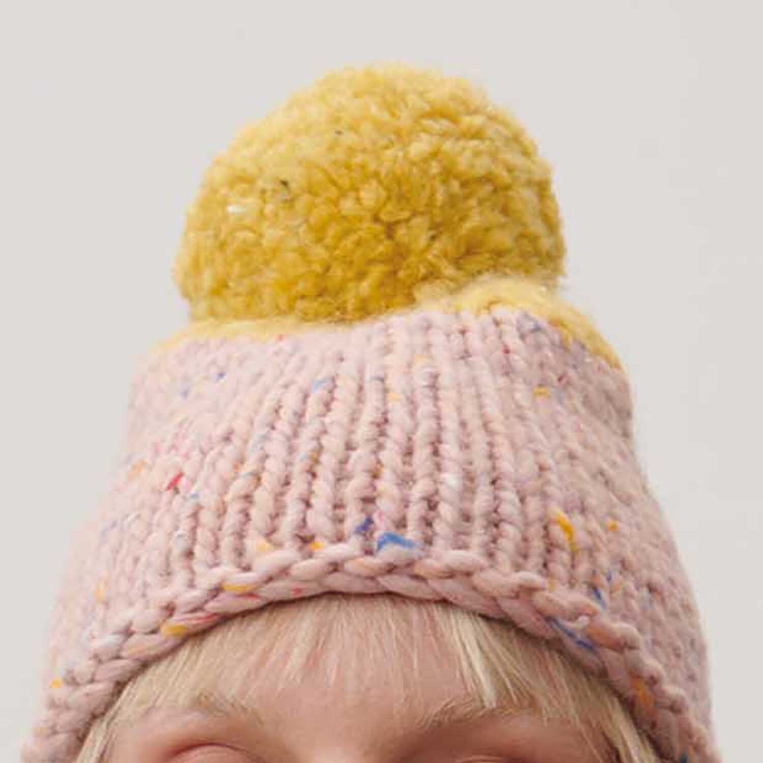 Essentials Super Tweed super chunky Mütze in Puder mit gelbem Bommel, gestrickt aus Rico Design Garn.