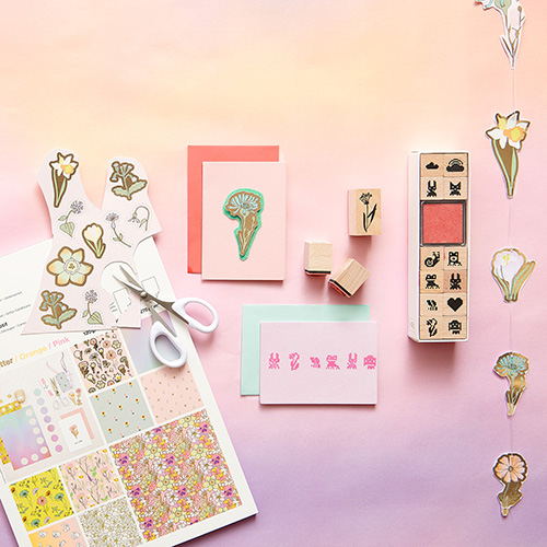 Ein Motivpapierblock, gestaltete Karten, ein Stempelset und eine genähte Girlande mit Papierblumen. Flatlay von Produkten aus der Kollektion Futschikato.