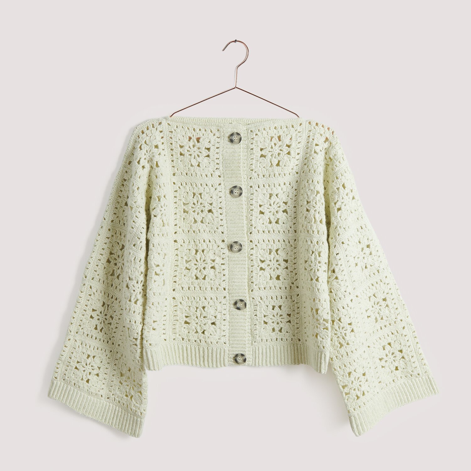 Häkelset Jacke Modell 01 B aus Die Neue Masche No. 15, cremefarbene Strickjacke mit Knöpfen und floralem Muster, auf einem Kleiderbügel.