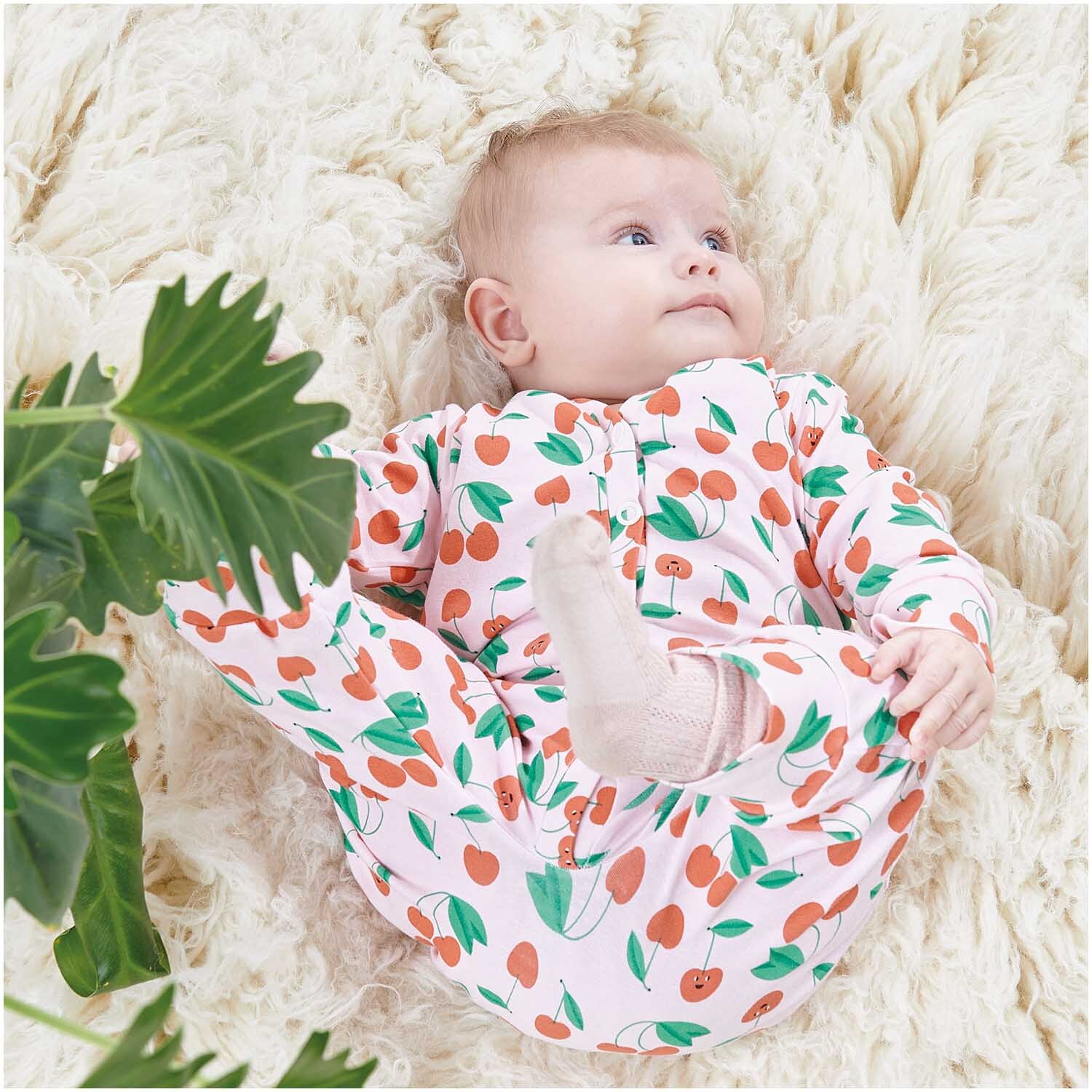 Stoffabschnitt Jersey bedruckt Kirschen rosa 80x100cm: Baby in Kirschmuster-Outfit auf weichem, cremefarbenem Teppich liegend.