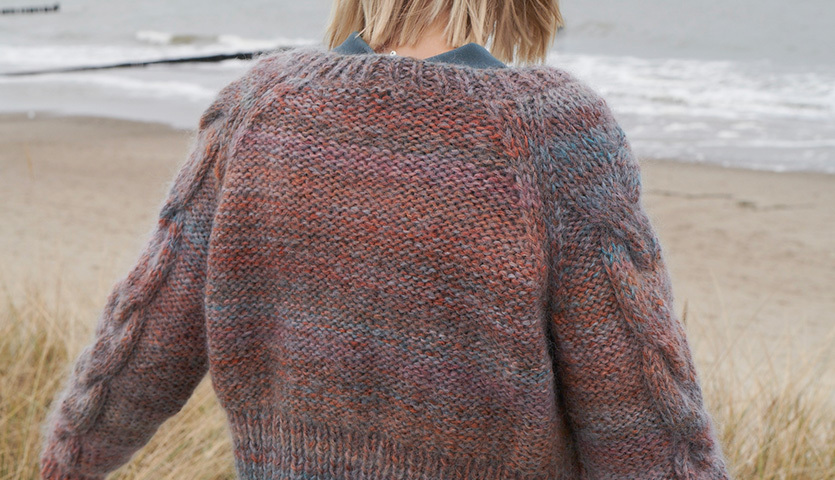Strickanleitung Jacke aus Creative Mohair Melange: Frau am Strand in bunter Strickjacke aus Mohair, Rückenansicht.