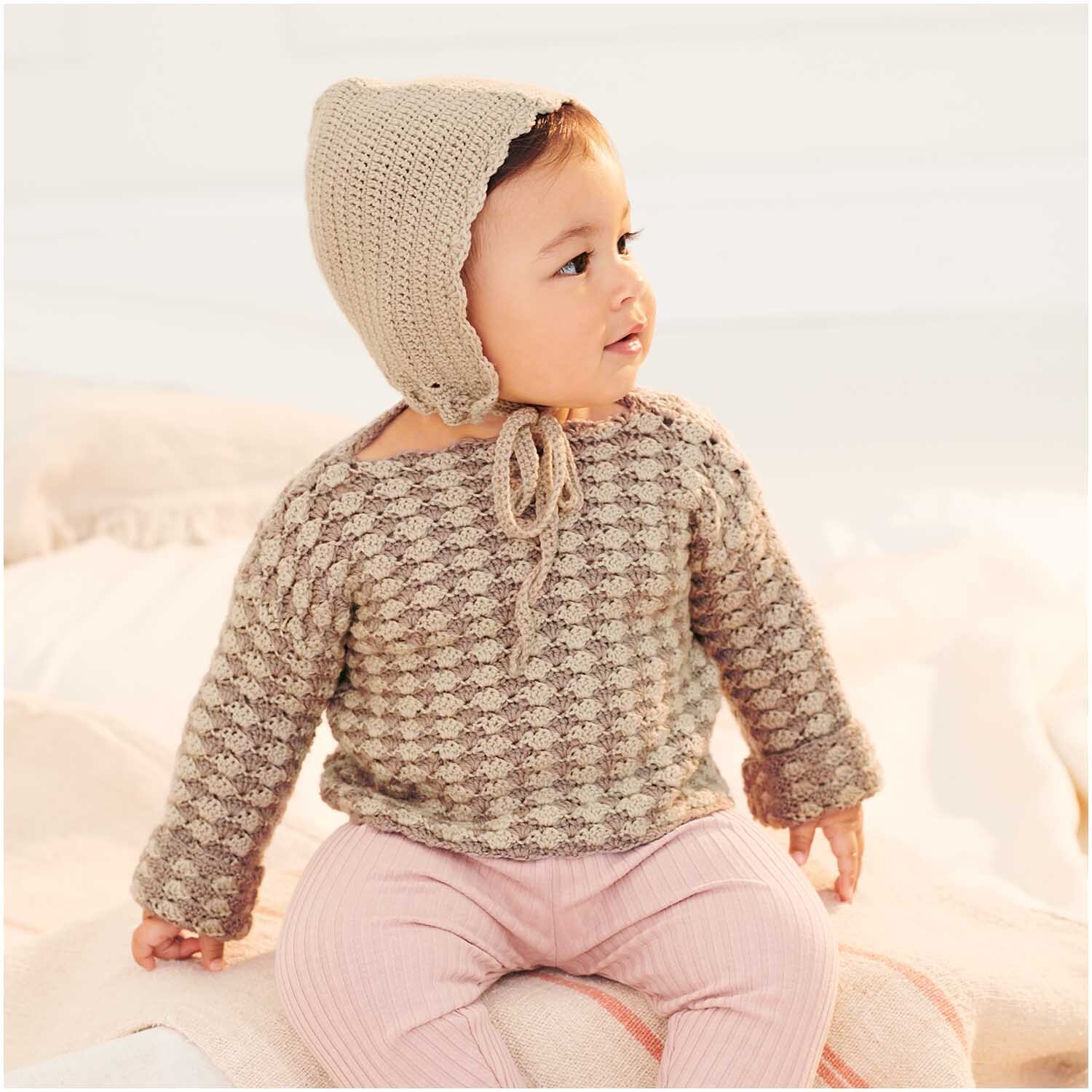 Baby Merino: Ein Baby trägt einen gestrickten Pullover und eine passende Mütze in Beige. Perfekt für kühle Tage.