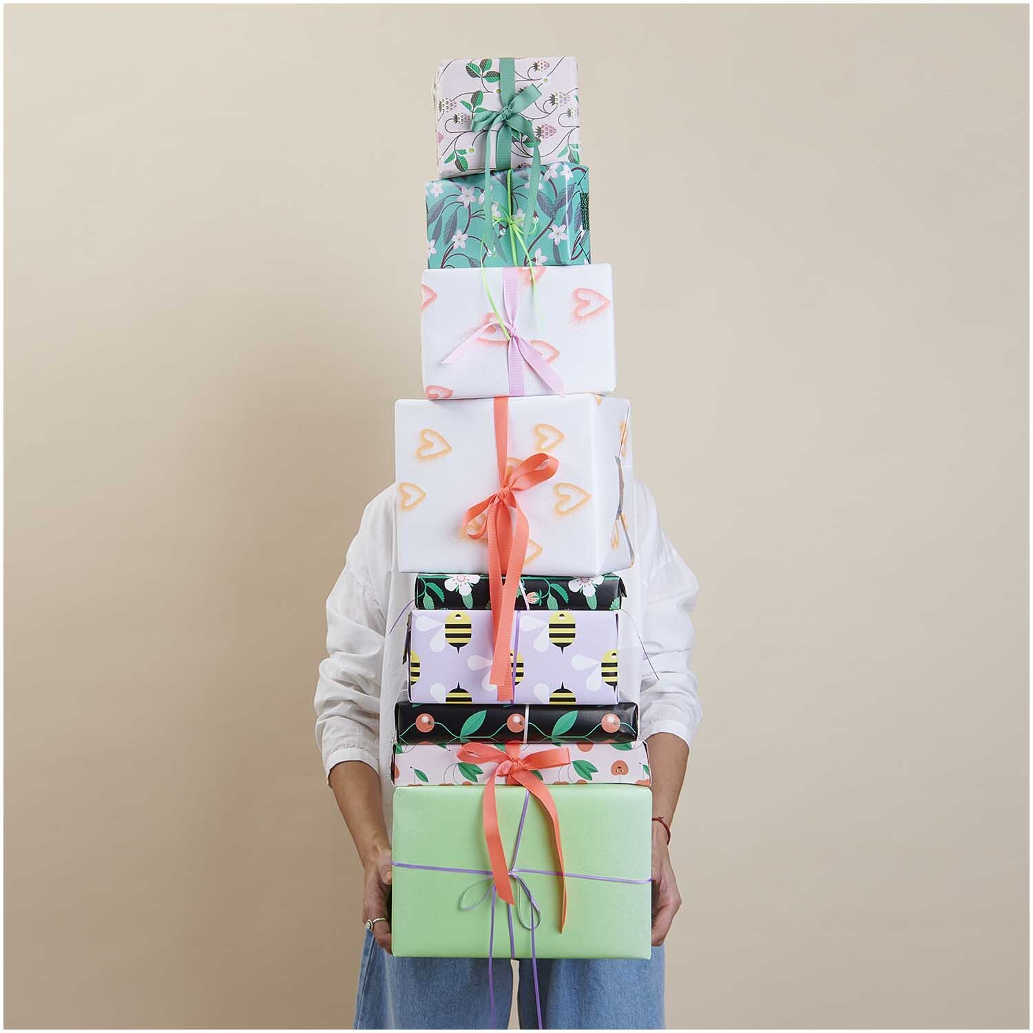 Paper Poetry Geschenkpapier zeigt bunte, gestapelte Geschenke mit Herzen und Schleifen. Ideal für kreative Verpackungen.
