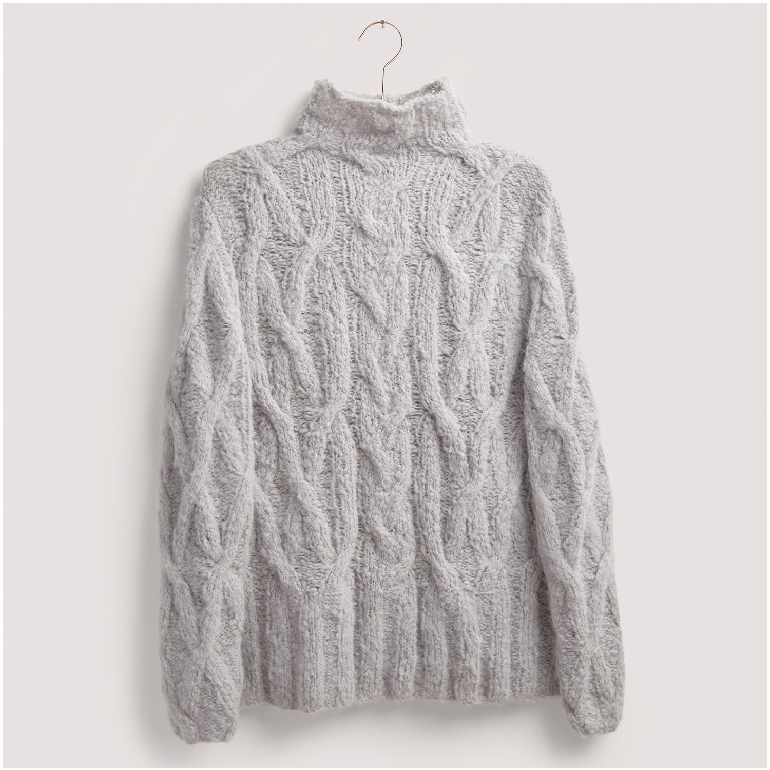 Strickset Pullover Modell 28 aus Die Neue Masche Nr. 8: Weicher, grauer Zopfmuster-Pullover mit Rollkragen, hängend an einem Haken.