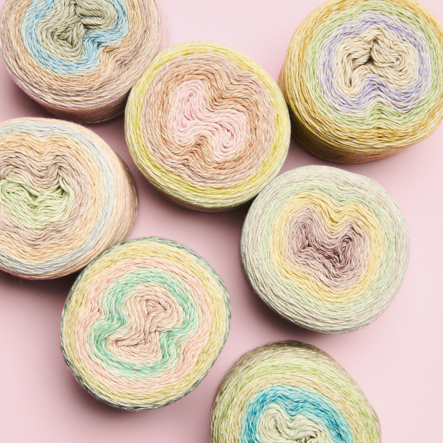Creative Cotton Linen Cake Sortiment I 35-teilig, pastellfarbene Garnrollen auf rosa Hintergrund.