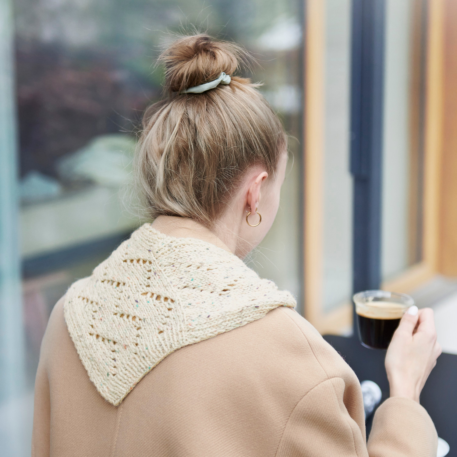 Strickset Mini Tuch Modell 10: Frau mit beigem Stricktuch, hält eine Tasse Kaffee, trägt beigen Mantel.