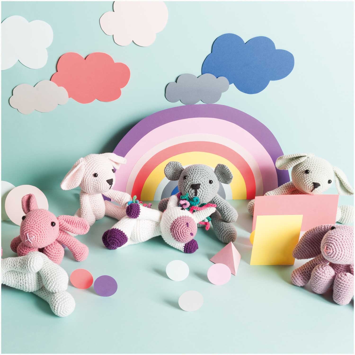 Creative Ricorumi dk: Bunte Häkeltiere vor Regenbogenkulisse, umgeben von pastellfarbenen Wolken und Formen. Ideal für kreative DIY-Projekte.