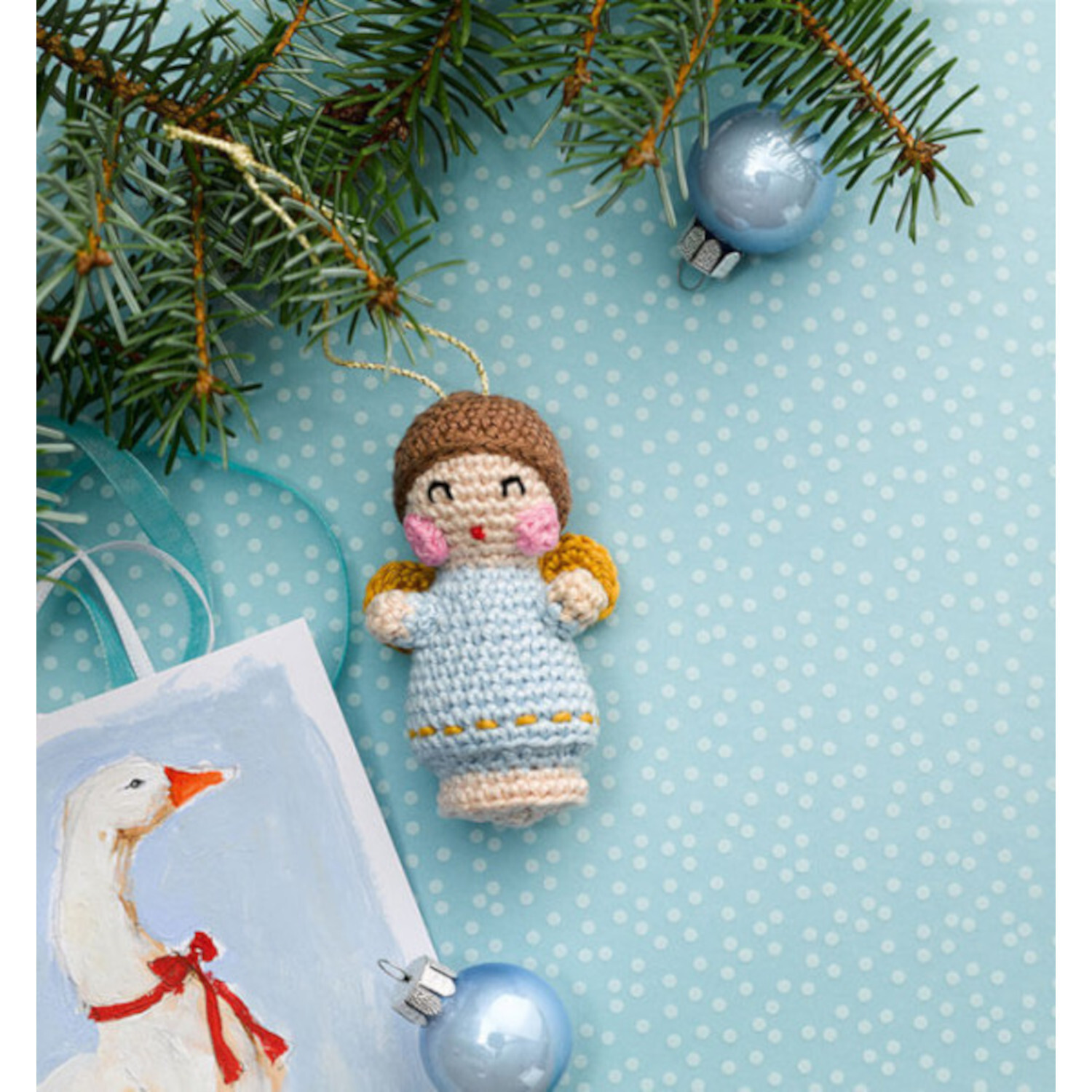 Christmas Cuteness. Baumschmuck häkeln - Adventskalender: Niedlicher gehäkelter Engel in Blau mit goldenen Flügeln, umgeben von Tannenzweigen und blauen Kugeln.