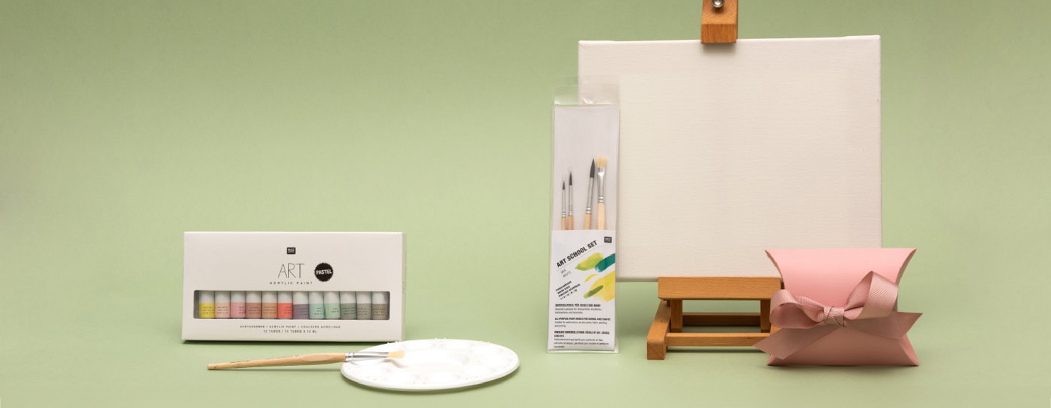 Leinwand auf Tischstaffelei mit Pinsel und Farben in der Verpackung, sowie eine Malpalette und Geschenkschachtel. Fotosetting grüne Wand.