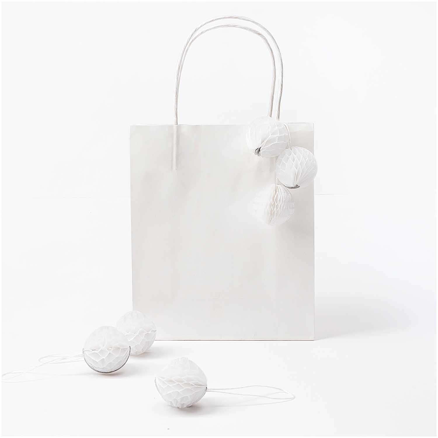 Mini-Wabenbälle 4cm 6 Stück von Rico Design, dekorativ an einer weißen Geschenktüte befestigt.