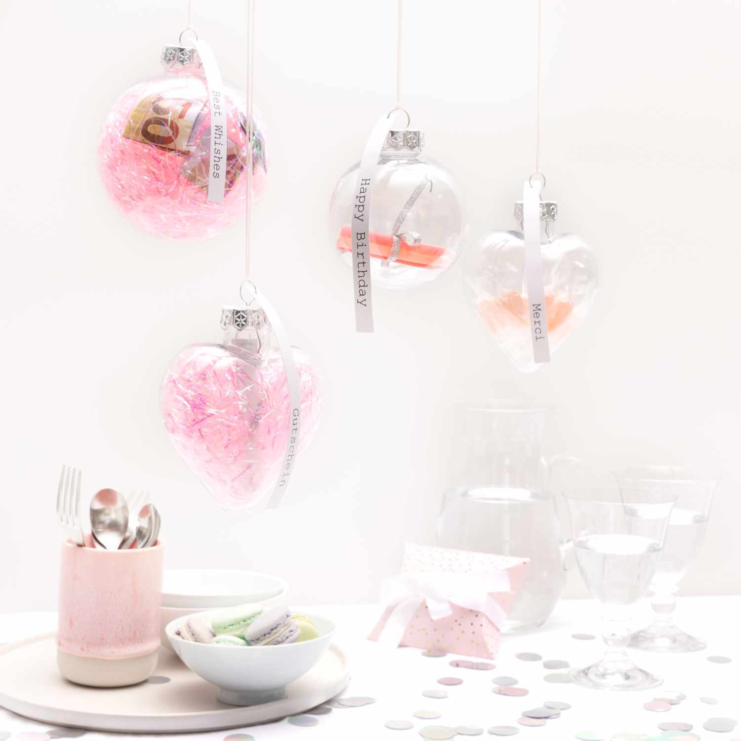 Weihnachtskugel aus Kunststoff 10cm, dekoriert mit rosa Füllung, hängt neben weiteren transparenten Kugeln.