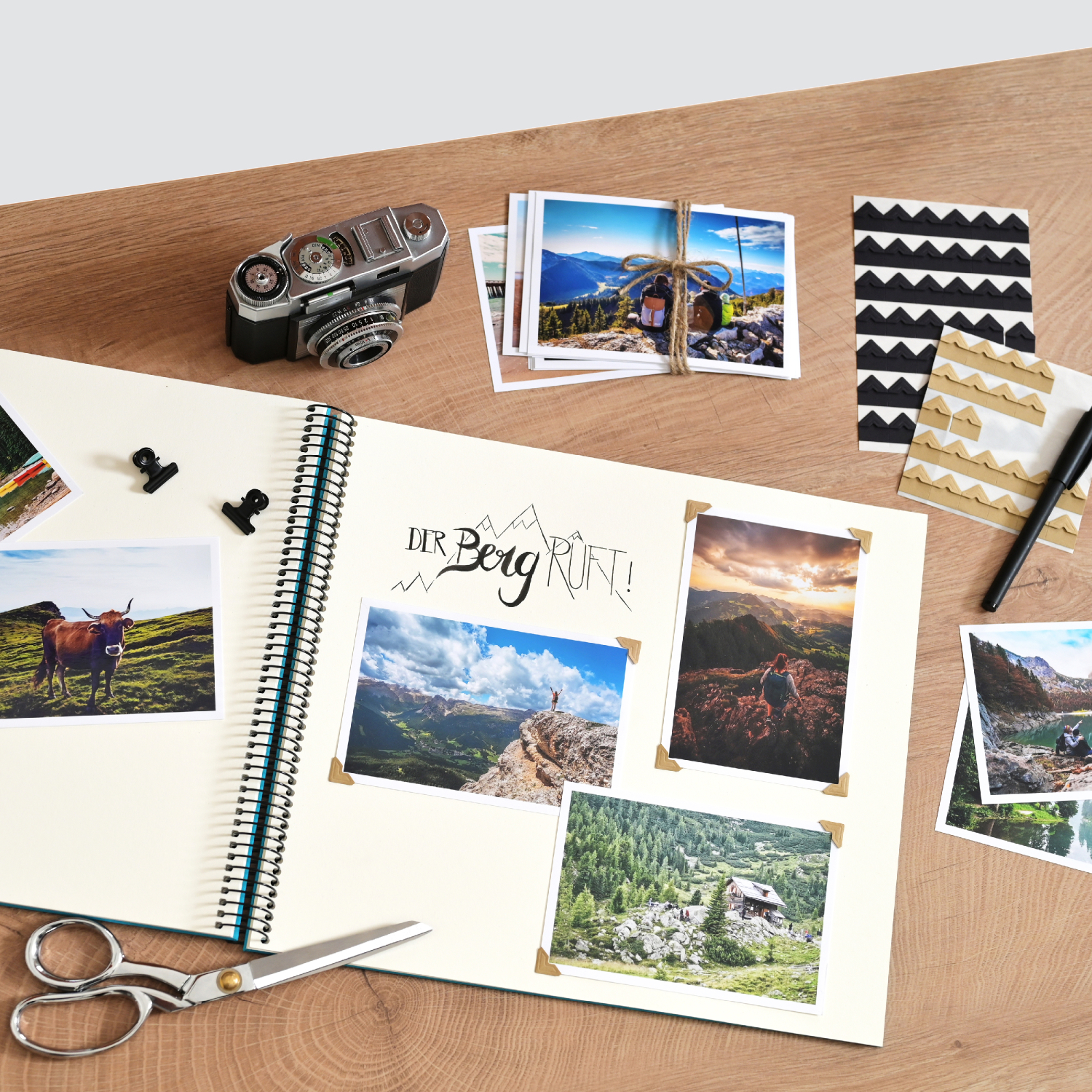 Fotoecken Crea: Offenes Fotoalbum mit Landschaftsbildern, Kamera, Schere und Fotoecken auf Holztisch.