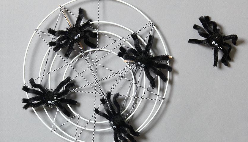 Bastelanleitung Halloween- Spinnennetz: Schwarze Spinnen aus Pfeifenreinigern auf weißem Netz.