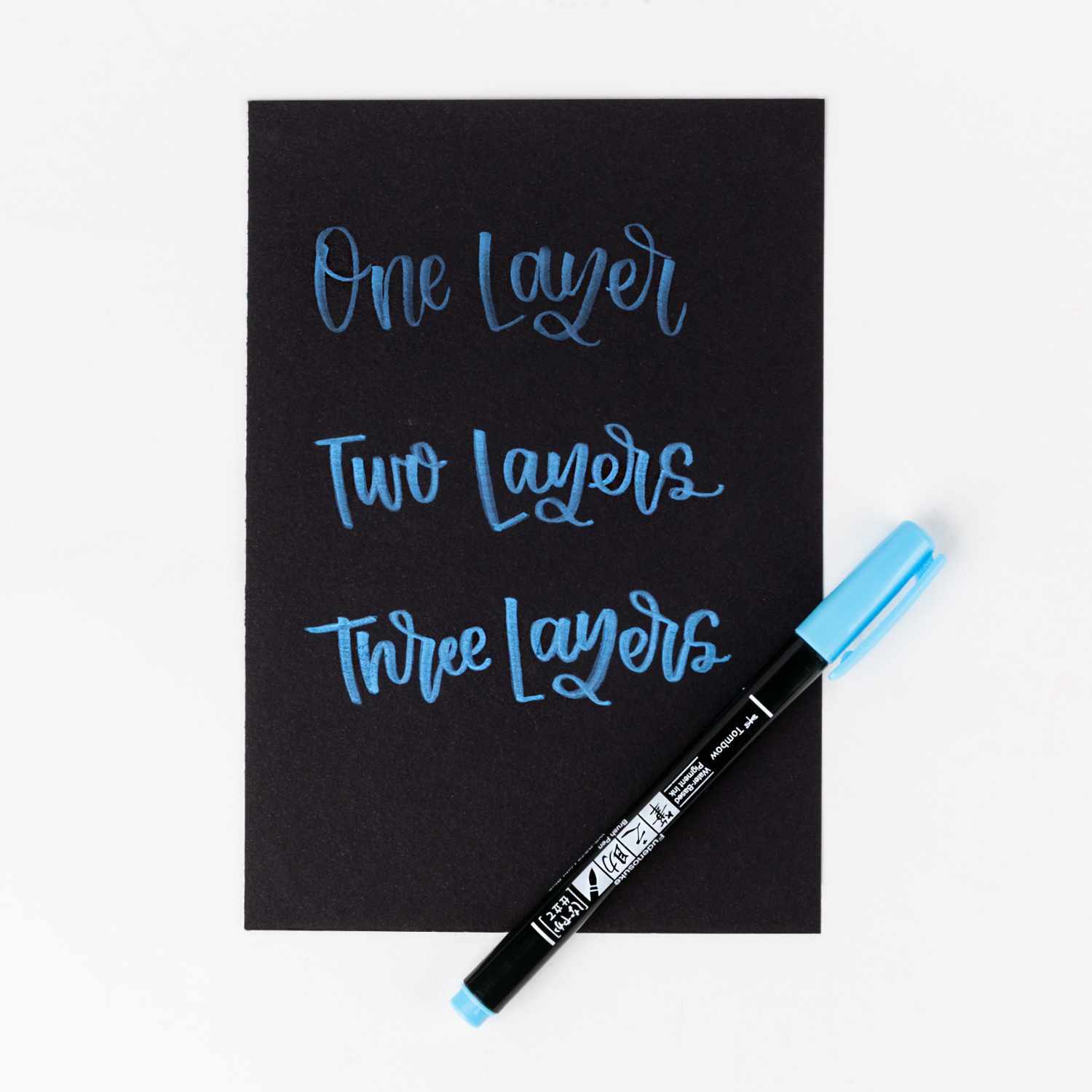 Fudenosuke Brush Pen Pastel von Tombow in Hellblau auf schwarzem Papier mit Schriftproben.