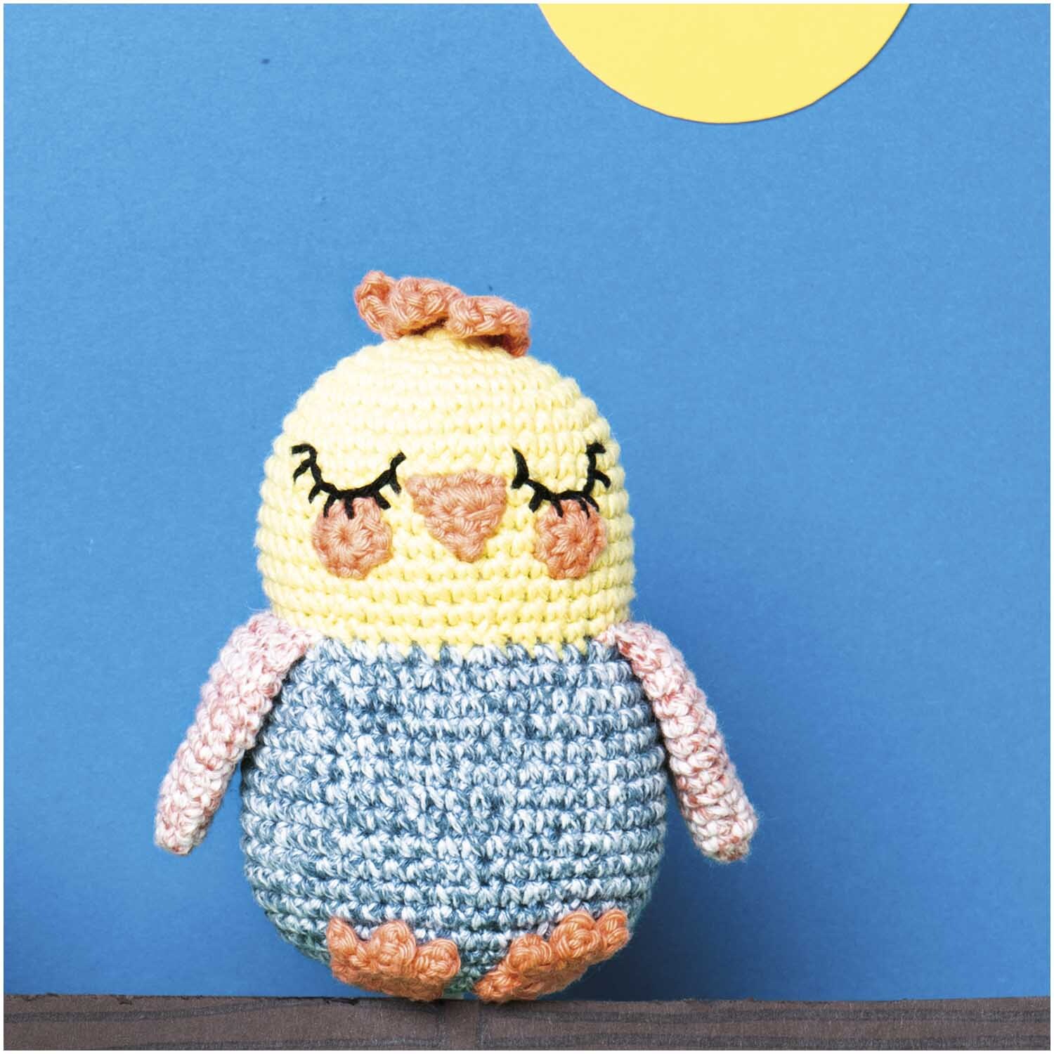 Creative Ricorumi dk Set Limited: Gehäkeltes Küken mit geschlossenen Augen vor blauem Hintergrund.