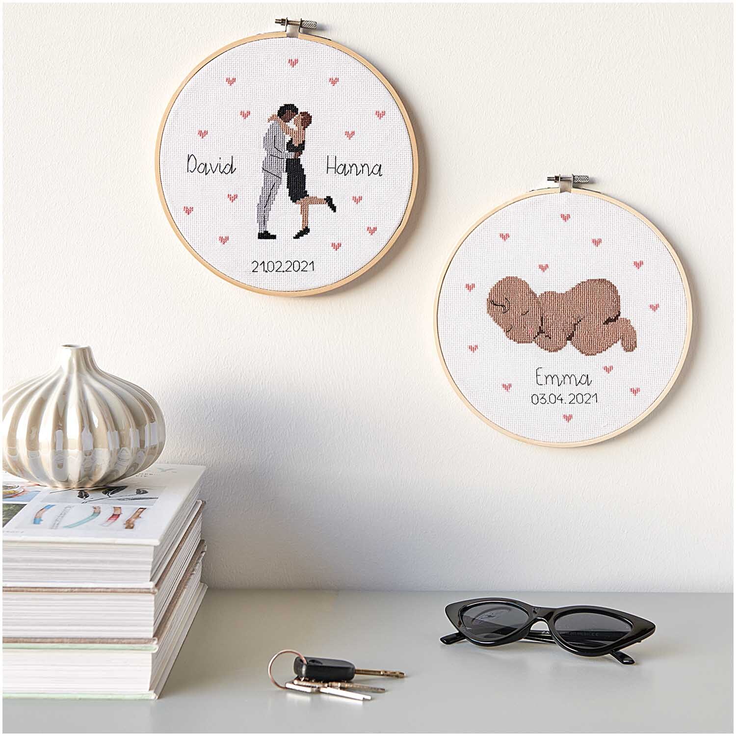 Figurico Stickpackung Baby 20cm zeigt zwei bestickte Rahmen mit Paar und Baby, umgeben von Herzen. Ideal für personalisierte Geschenke.