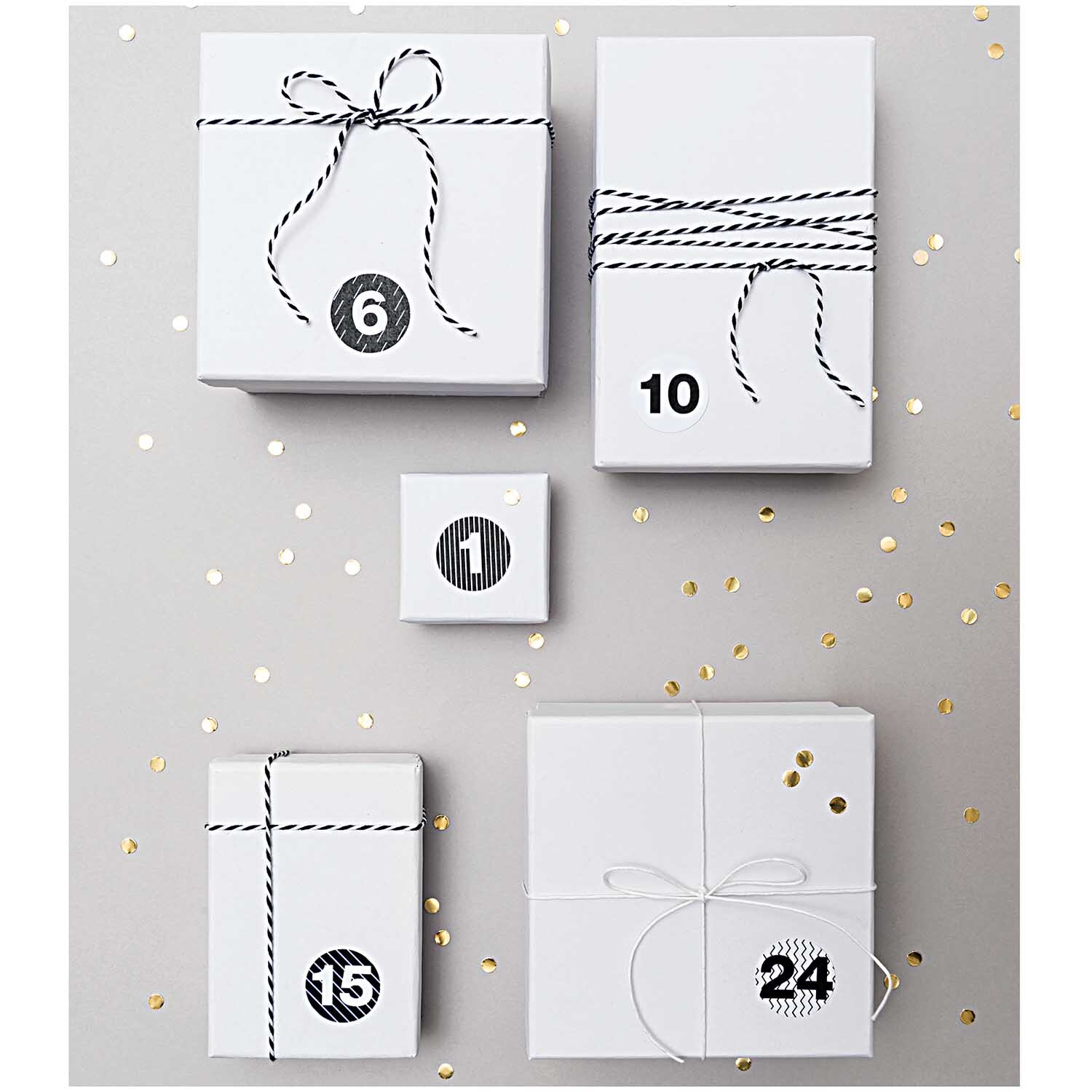 Paper Poetry Baumwollgarn schwarz-weiß 15m von Rico Design, dekorativ um weiße Geschenkboxen gewickelt, auf grauem Hintergrund mit goldenen Punkten.