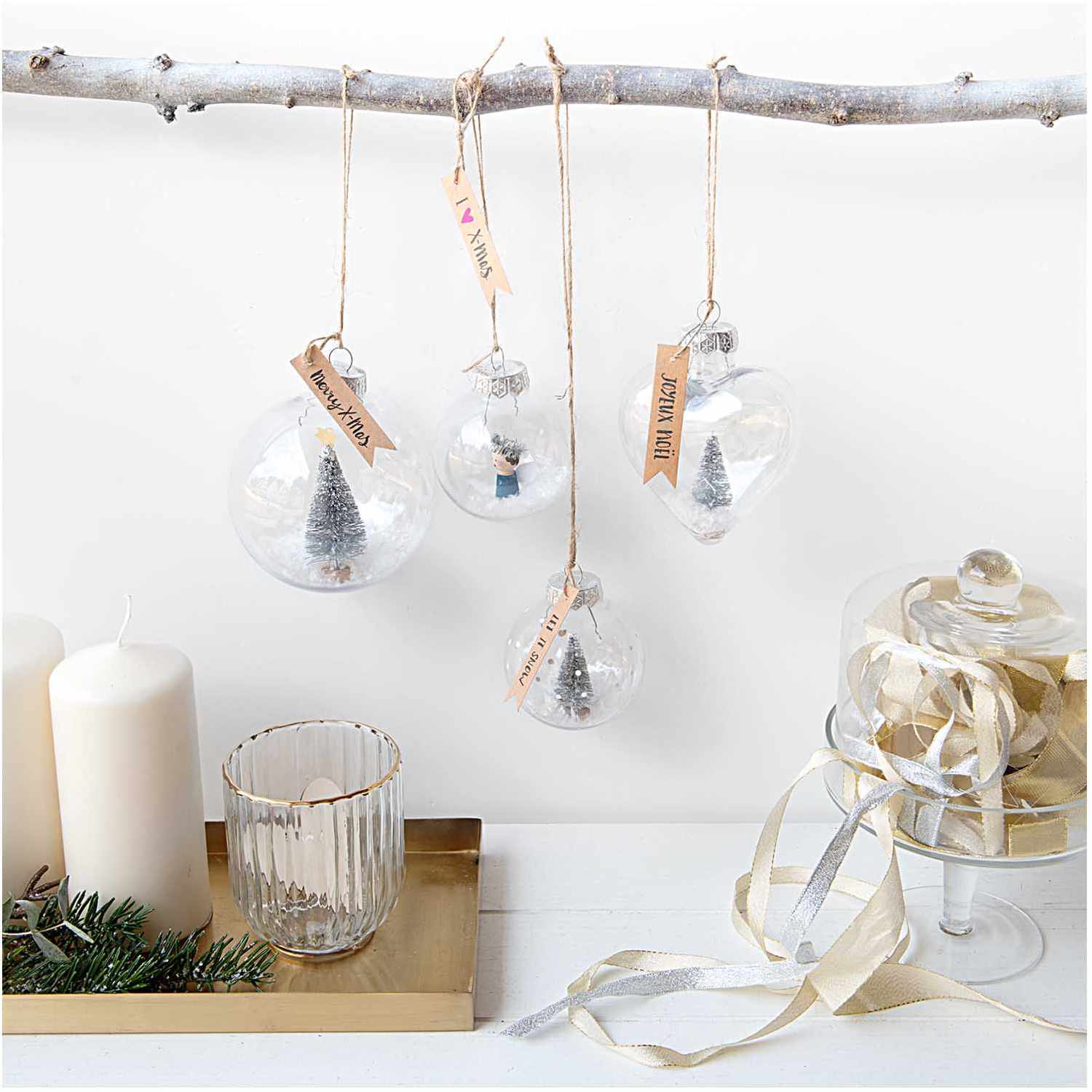 Weihnachtskugel aus Kunststoff 7cm, transparent, von Rico Design, hängt an einem Ast mit weiteren Dekorationen.