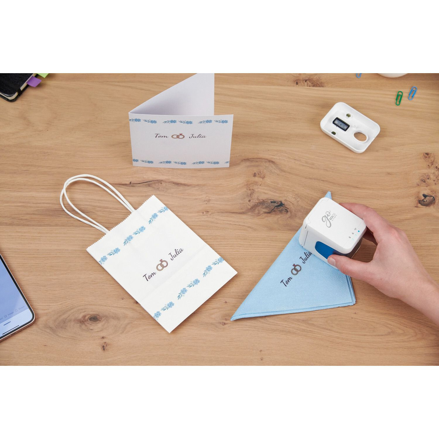 e-mark GO Bundle inkl. Tintenpatrone: Person stempelt blaues Tuch auf Holztisch, daneben Geschenktüte und Karte.