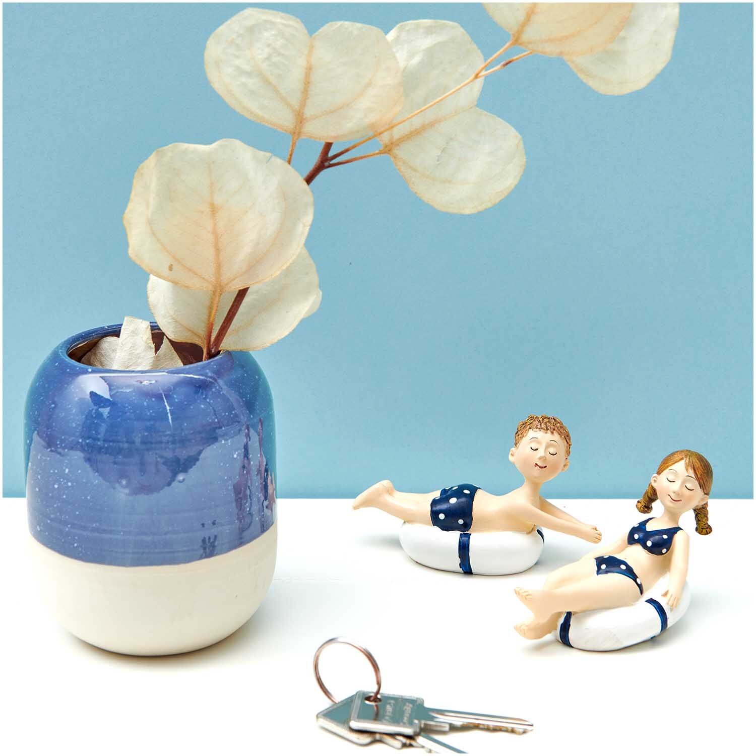 Deko-Figur Junge mit Schwimmreifen neben Mädchenfigur, beide in blauen Badeanzügen, vor blauem Hintergrund.