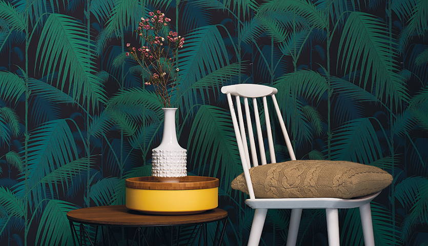 Strickanleitung Kissen aus Linea Botanica: Ein stilvolles Wohnzimmer mit einem weißen Stuhl, einem gemusterten Kissen und einem Tisch mit Vase vor tropischer Tapete.