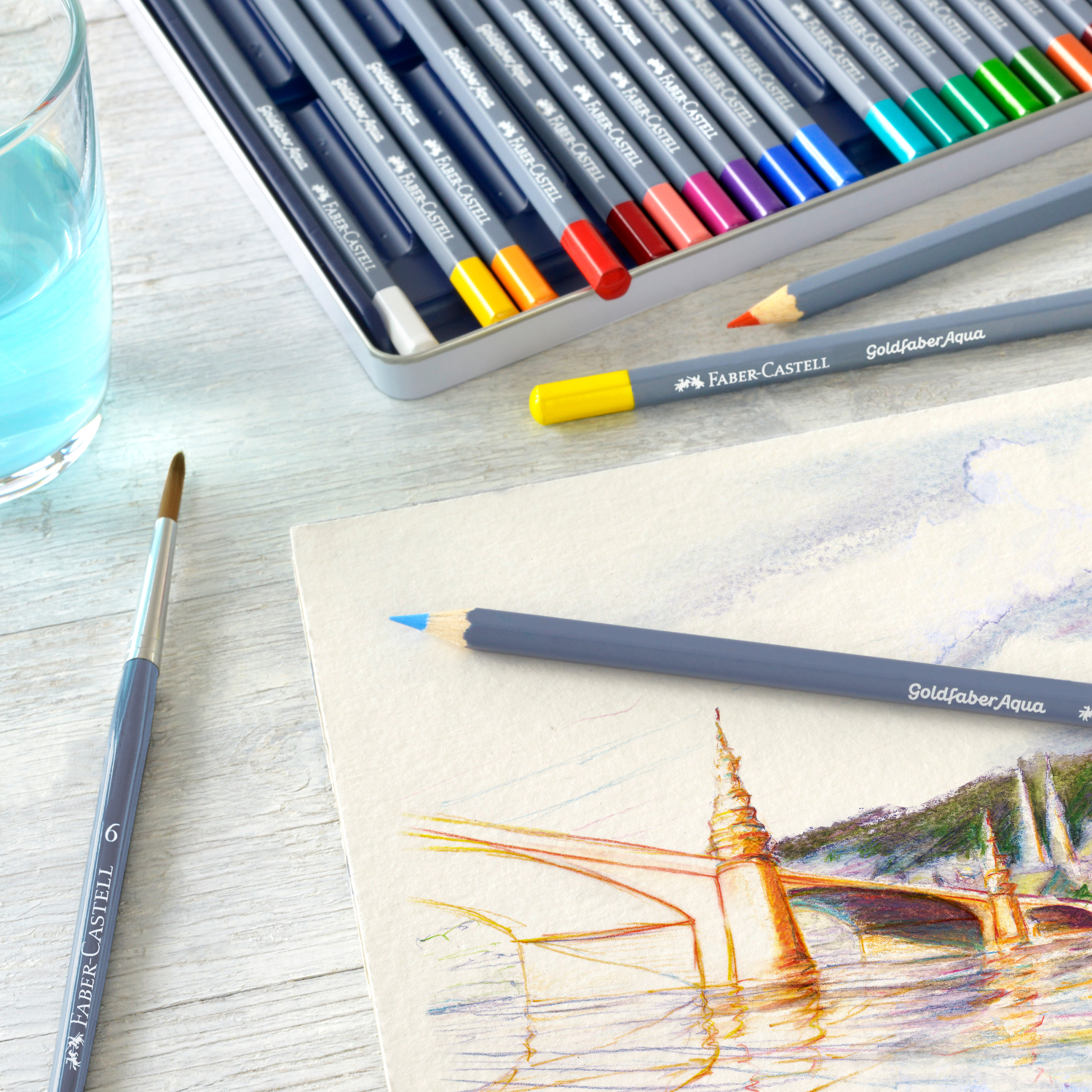 Goldfaber Aqua Aquarellstifte, 36-teilig, im Metalletui von Faber Castell, neben einem Aquarellbild und Pinsel auf einem Tisch.
