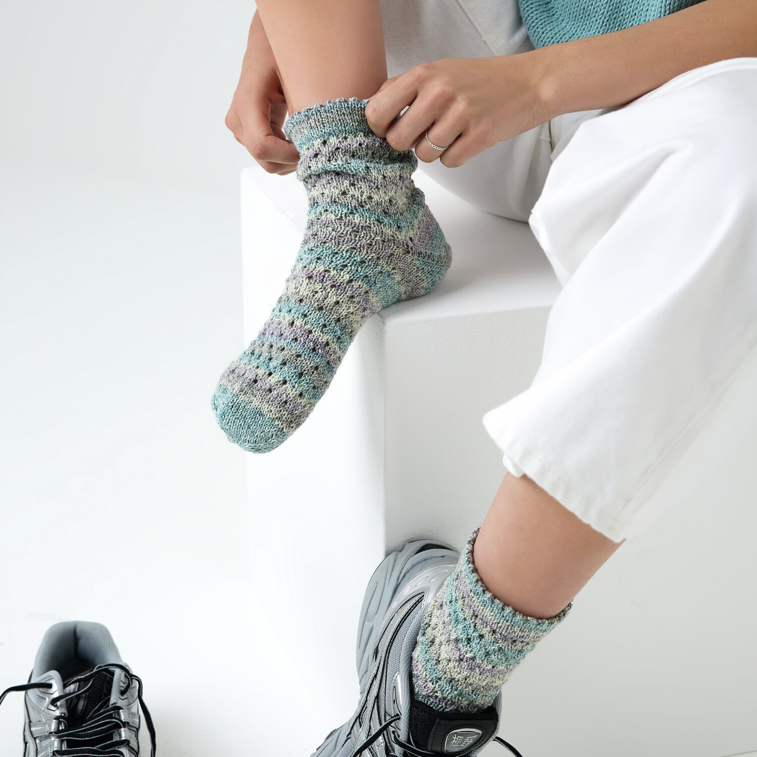 Strickset Socken Modell 14a: Person trägt gestrickte, bunte Socken mit weißer Hose und grauen Schuhen.