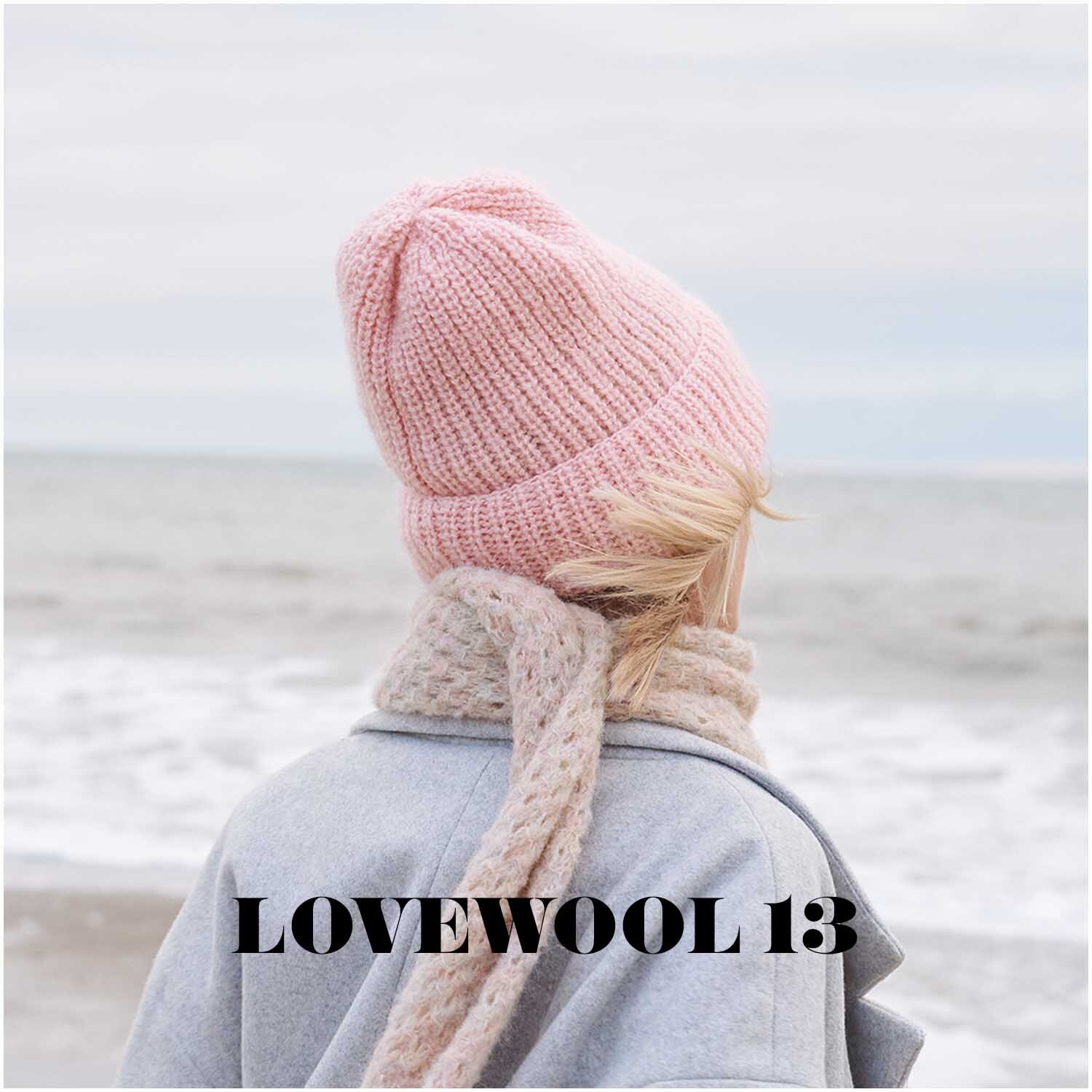 Luxury OMG: Frau am Strand mit rosa Mütze und Schal von Rico Design, Blick aufs Meer.