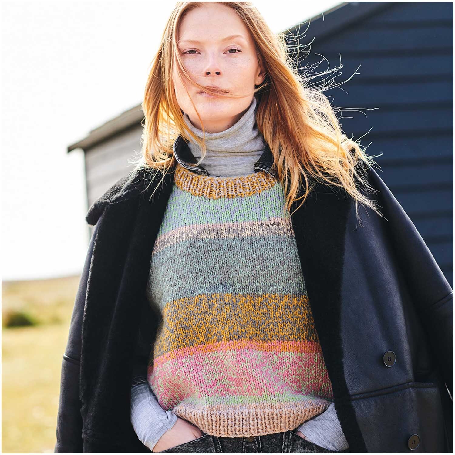 Creative Chic-Unique Pullover in Streifenmuster, getragen von Frau im Freien, kombiniert mit schwarzem Mantel.