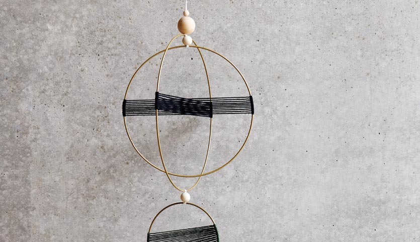 Anleitung Makramee-Mobilé: Elegantes, handgefertigtes Mobilé mit goldenen Ringen und schwarzen Fäden.