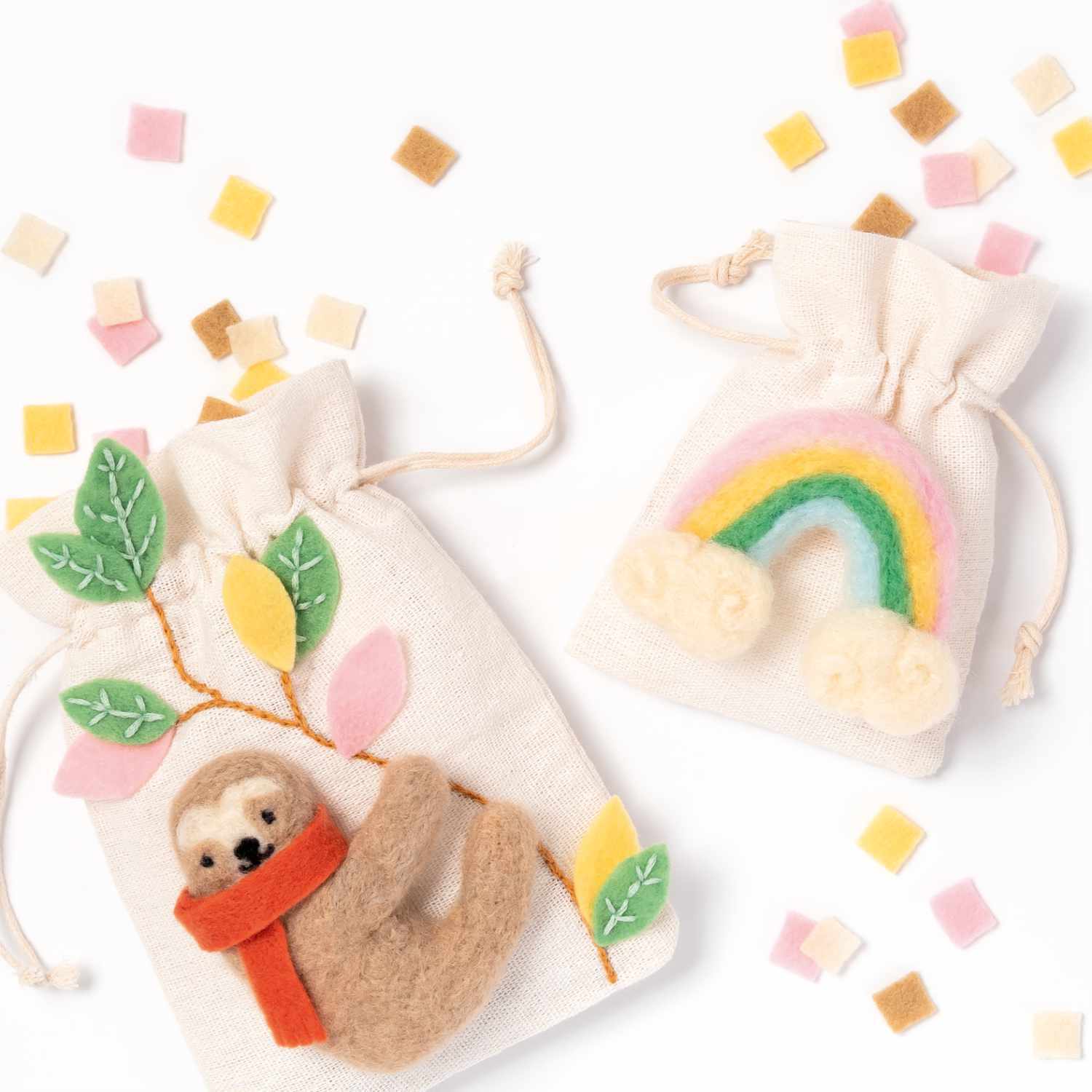 Filz-DIY-Box: Zwei kreative Filzbeutel mit Faultier- und Regenbogenmotiv, umgeben von bunten Filzstücken.