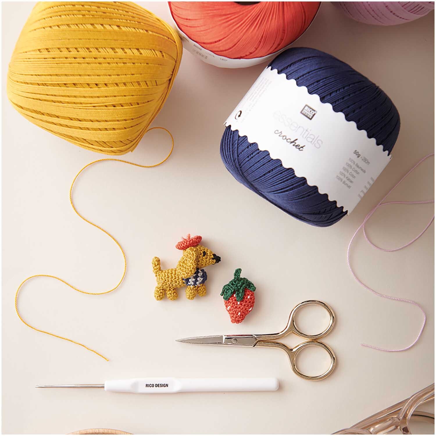 Essentials Crochet: Bunte Häkelgarne, Häkelnadel und Schere auf Tisch, ideal für kreative Projekte.