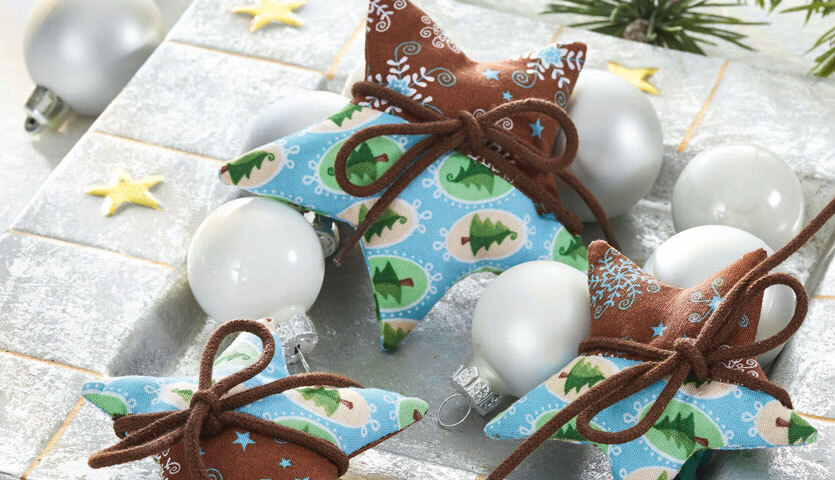 Nähanleitung Stoffsterne: Handgefertigte Stoffsterne in Blau und Braun mit weihnachtlichen Mustern, dekoriert mit Schleifen und Kugeln.