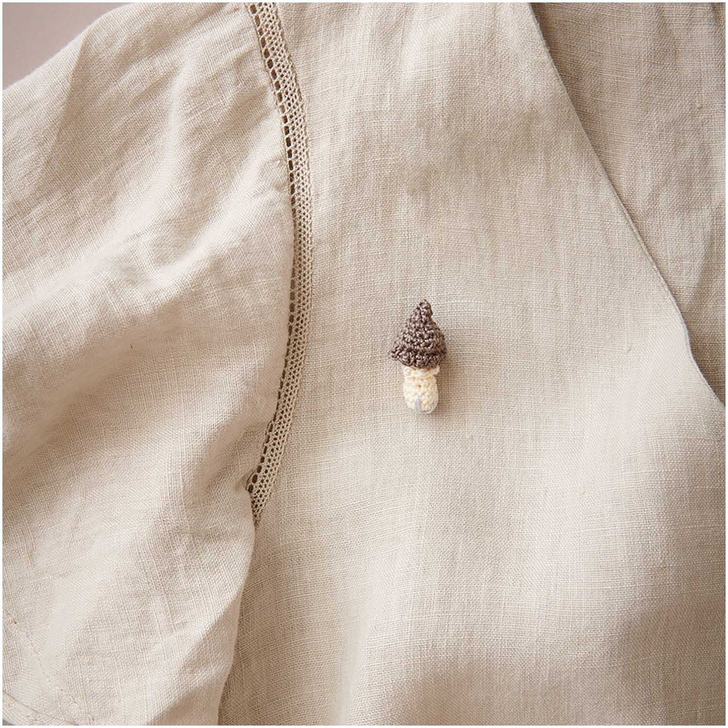 Essentials Crochet: Handgefertigter Pilz-Anstecker auf beiger Leinenbluse, ideal für kreative Akzente.