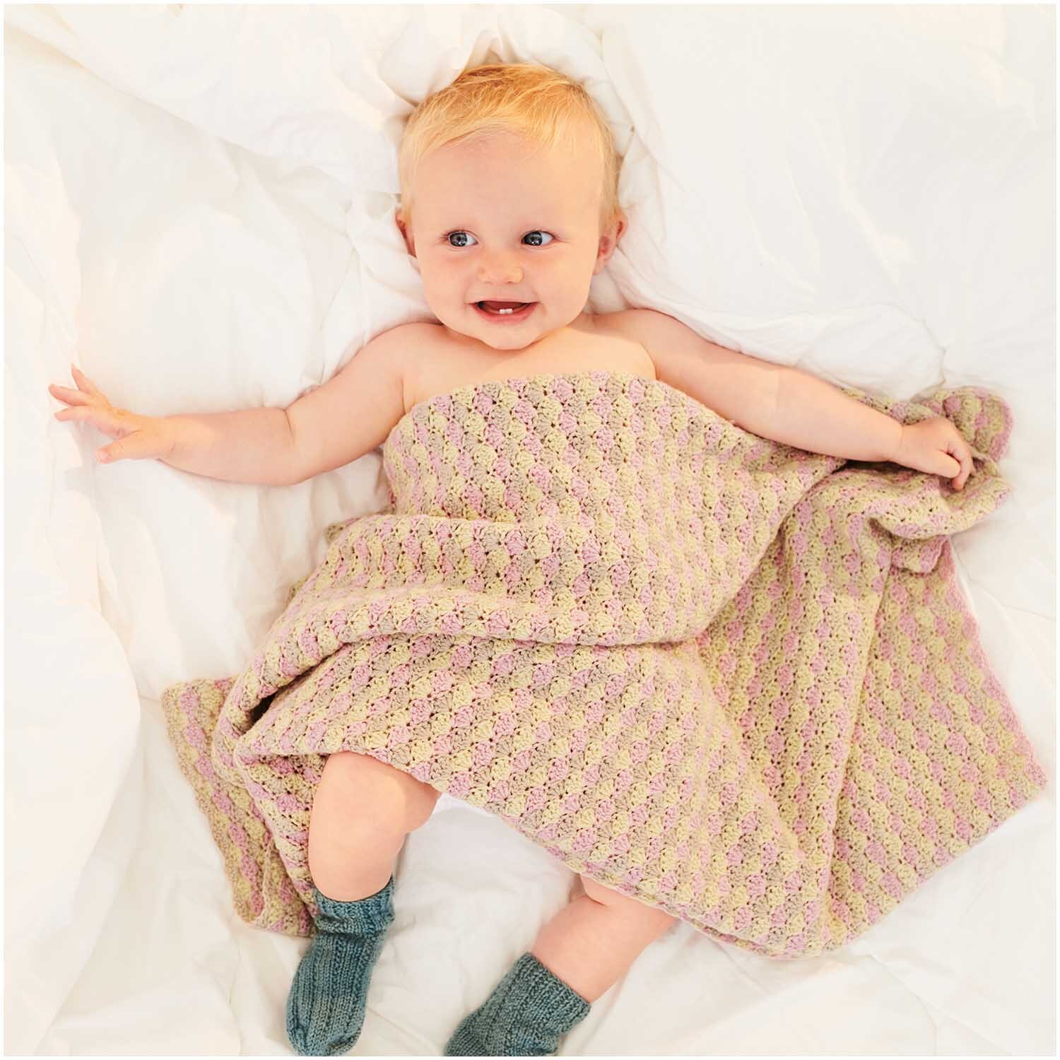 Baby Merino: Ein lächelndes Baby liegt in einer weichen, gestrickten Decke von Rico Design.